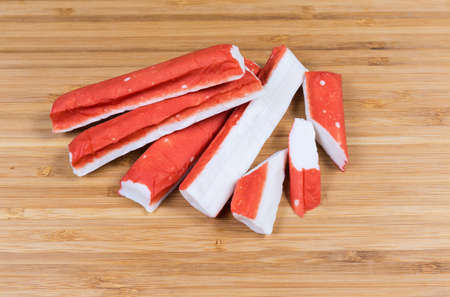 Pile of whole and slised crab sticks on a wooden bamboo cutting board close-upの写真素材