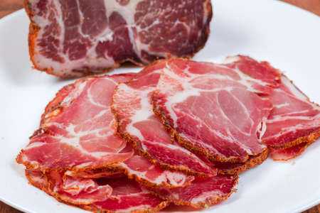 Sliced dried pork neck against of the unsliced rest of the piece on white dish close-up at selective focusの写真素材
