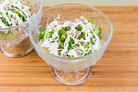 Fish salad of canned cod livers in own oil with boiled vegetables sprinkled with chopped green onion in two glass salad bowls on wooden surfaceの写真素材