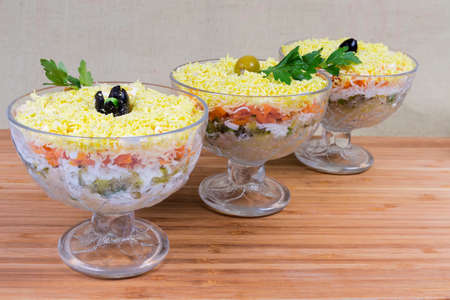 Salad made of canned fish, grated cheese, boiled eggs and vegetables, sprinkled with crumbled egg yolk called as mimosa salad in glass salad bowls on a wooden surfaceの写真素材