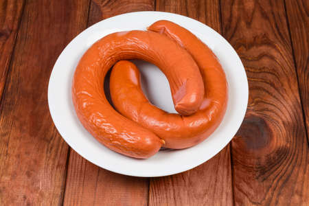 Two ring pork bologna sausages in natural casing on the white dish on dark colored wooden rustic...