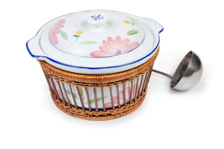 Vintage ceramic soup tureen with lid in special thermal insulation wicker wooden basket against of stainless steel ladle on a white backgroundの写真素材