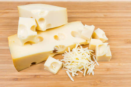 Partly sliced and grated Swiss-type cheese with large holes known as cheese's eyes on a bamboo...