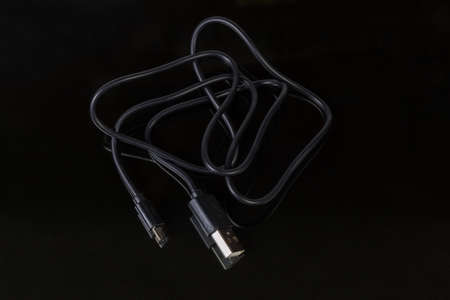 Black cable with plugs USB standard A and micro-USB standard B at the edges at selective focus on a...