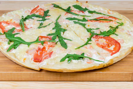 Cooked round pizza with shrimps, tomatoes and arugula on the bamboo cutting board close-up at selective focusの写真素材