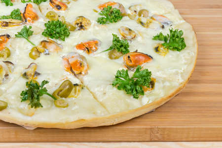 Fragment of the cooked round pizza with mussels, green olives and parsley on the bamboo cutting boardの写真素材