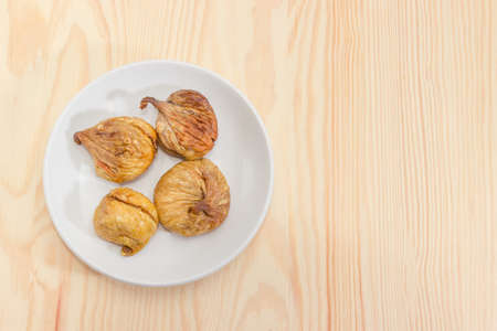 Top view of the dried fig fruits on the white saucer located left on a light colored wooden surfaceの写真素材