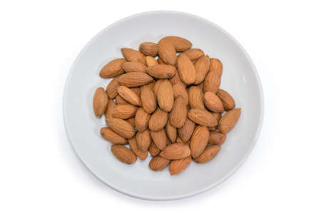 Top view of the dried almonds peeled from shells on the white saucer close-up on a white backgroundの写真素材