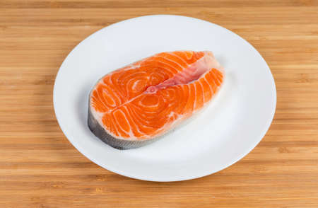 Fresh uncooked steak of arctic char on white dish on the bamboo wooden surfaceの写真素材