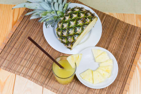Top view of pineapple juice in glass with drinking straw among of pineapple slices on saucer and...