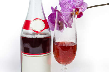 Fragment of bottle and wineglass with red sparkling wine against pink flowers of orchid close-up on a white backgroundの写真素材