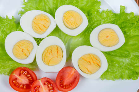 Top view of the halves of boiled chicken eggs and cherry tomatoes on lettuce leaves on white dish...