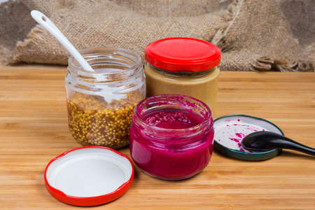Various condiments - traditional mustard, French whole-grain mustard and horseradish sauce with red...