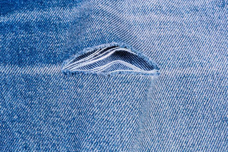 Hole on blue  jeans. Texture of the old torn denim showing the frayed threads, fragment close-up