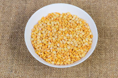 Raw the split peas of yellow variety in white bowl on a sackcloth surface
