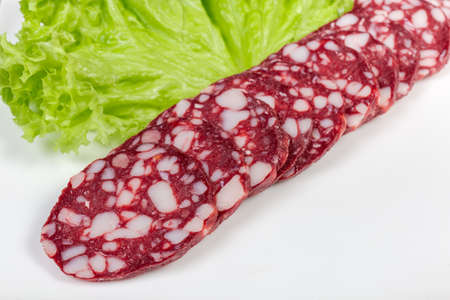 Sliced dry-cured sausage made from beef and pork on dish with lettuce leaf close-up in selective focusの写真素材