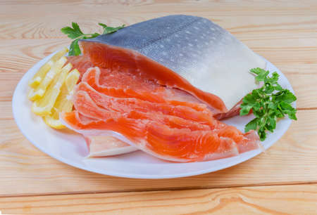 Pieces of arctic char fillet on skin and several slices same fish, slices lemon and parslet on white dish on the wooden rustic tableの写真素材
