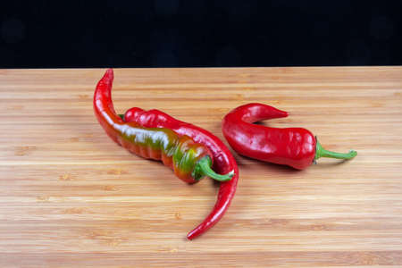 Several fresh red and red-green pepper chili on a bamboo wooden surface on black background close-up...