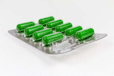 Blister pack with pharmaceutical drug in the form of green capsules with one used capsule on a light table close-up in selective focusの写真素材