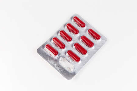 Blister pack with pharmaceutical drug in the form of red capsules with one used capsule on a light colored table, top viewの写真素材