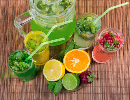 Cold mint drinks with various freshly squeezed citrus and strawberry, some ingredients on the bamboo...