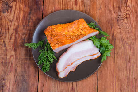 Partly sliced boiled smoked pork belly with skin on the brown dish with greens on the wooden rustic...