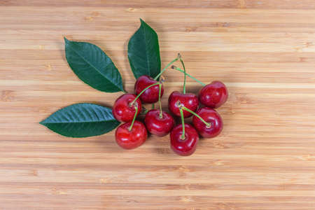 Ripe red sweet cherries with stalks and leaves close-up on a bamboo wooden surface, top view