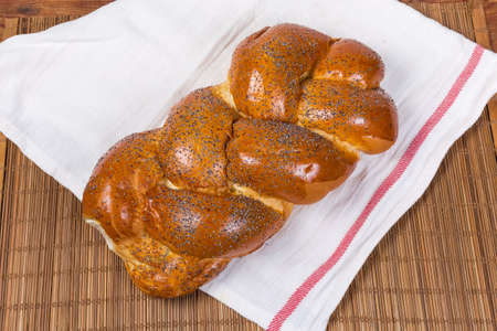 Whole sweet braided bread sprinkled with poppy seeds on the textile napkin on the bamboo table mat, top viewの写真素材
