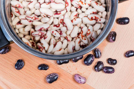 Uncooked soaked speckled red-white kidney beans in stainless steel cooking pot with water against of...