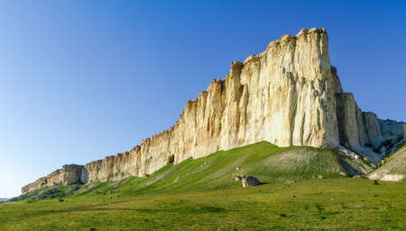 Steep white limestone rock on edge of the plateau on a background of clear sky, panoramic view from a foot of the mountの写真素材