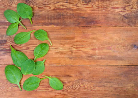 Surface of the old wooden rustic table with scattered fresh spinach leaves, located left and empty rest part. Top view, backgroundの写真素材