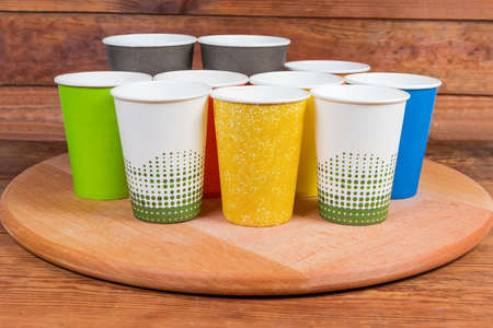 Empty disposable paper cups different sizes and colors on the round wooden serving board on rustic tableの写真素材
