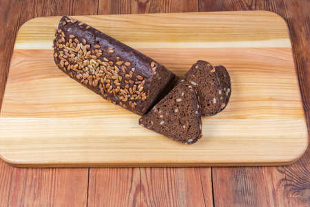 Partly sliced brown grain bread, triangular shape, sprinkled with sunflower seeds on the wooden...