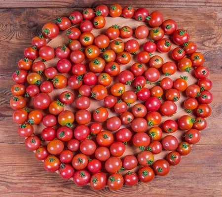 Cherry tomatoes laid out on the round wooden serving board on the rustic table, overhead viewの写真素材