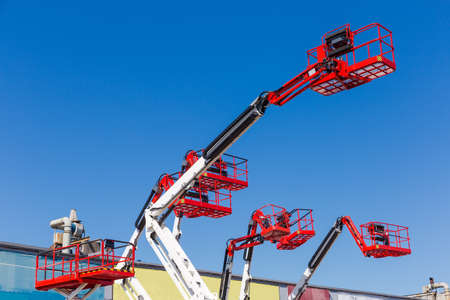 Fragment of the booms with baskets and top parts of different articulated boom lifts and scissor lifts on a background of clear skyの写真素材