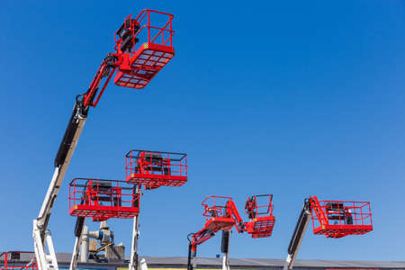 Red baskets on the white booms of different articulated boom lifts and top parts of lifts on a background of clear skyの写真素材
