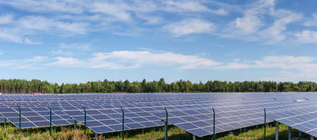Fragment of the ground-mounted solar power station with fixed photovoltaic arrays on a background of forest and sky, panoramic viewの写真素材