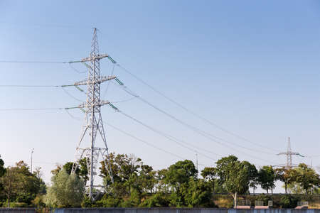 Steel lattice transmission tower of overhead power line on a background of trees and clear skyの写真素材