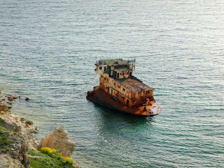 Old rusty hull part of the shipwrecked ship in water near the rocky sea shoreの写真素材