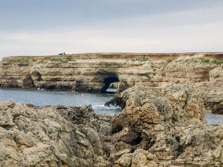 Section of the sea shore with textured limestone rocks and natural through grotto in promontoryの写真素材