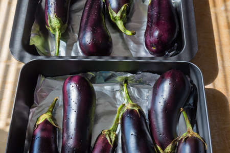 Whole eggplants with punctured peel with a fork, laid out on two oven trays covered with foil before baking, fragment close-up in selective focusの写真素材