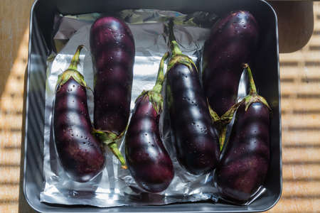 Whole eggplants with peel, punctured with a fork laid out on the oven tray covered with foil before baking, top viewの写真素材