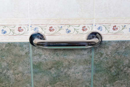 Horizontal grab bar made with stainless steel and mounted on wall with green and white tiles in a...