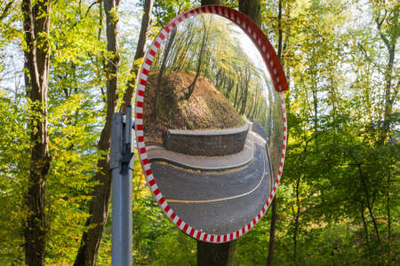 Convex spherical traffic panoramic mirror, mounted on a turn of road on a background of trees, reflection of the winding forest road in him 
の写真素材