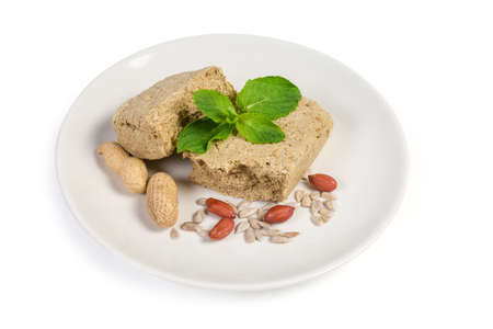 Pieces of the crumbly sunflower halva with peanuts addition, separately mint leaves, sunflower seeds, peeled and unpeeled peanuts on the dish on a white backgroundの写真素材