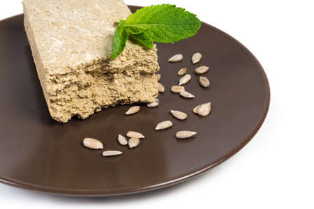 Crumbly halva, made with sunflower seeds, sugar, decorated with mint leaves,  separately peeled sunflower seeds on the brown dish on a white background, close-up in selective focusの写真素材