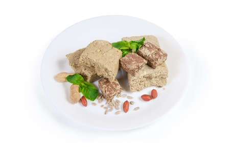 Various crumbly sunflower halva with peanuts, vanilla and cocoa powder addition decorated with mint twigs, peanuts and sunflower seeds on dish on a white backgroundの写真素材