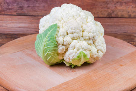Head of the fresh cauliflower on the round wooden serving board close-up in selective focusの写真素材