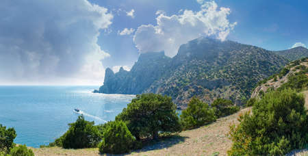 Section of the sea shore with steep rocks overgrown with juniper trees and coastal part of the sea...