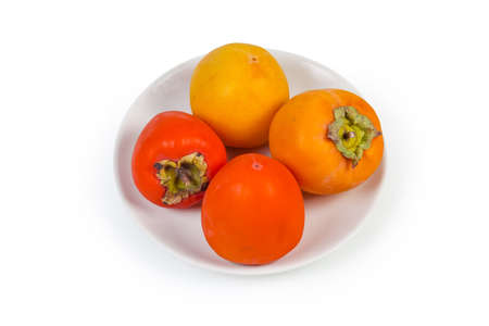 Fresh ripe whole persimmon fruits different varieties on the white dish on a white backgroundの写真素材